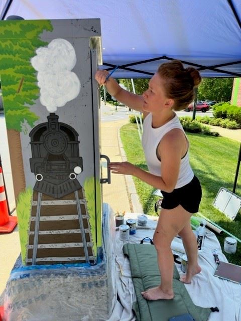 A young woman painting a switch box with a train image