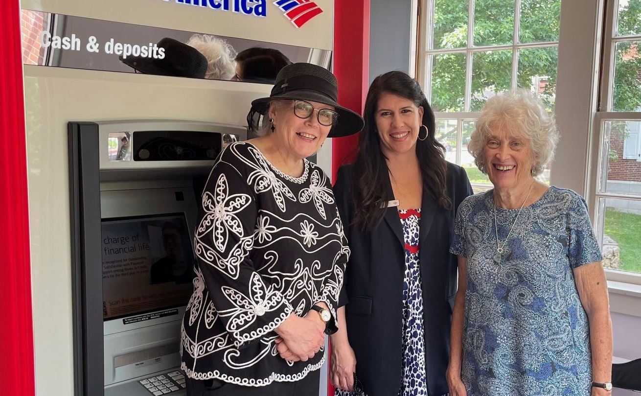 Two older women stand with the bank manager in front of the Bank of America ATM