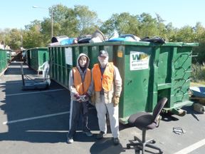 2 Men Standing Next to a Green Bin